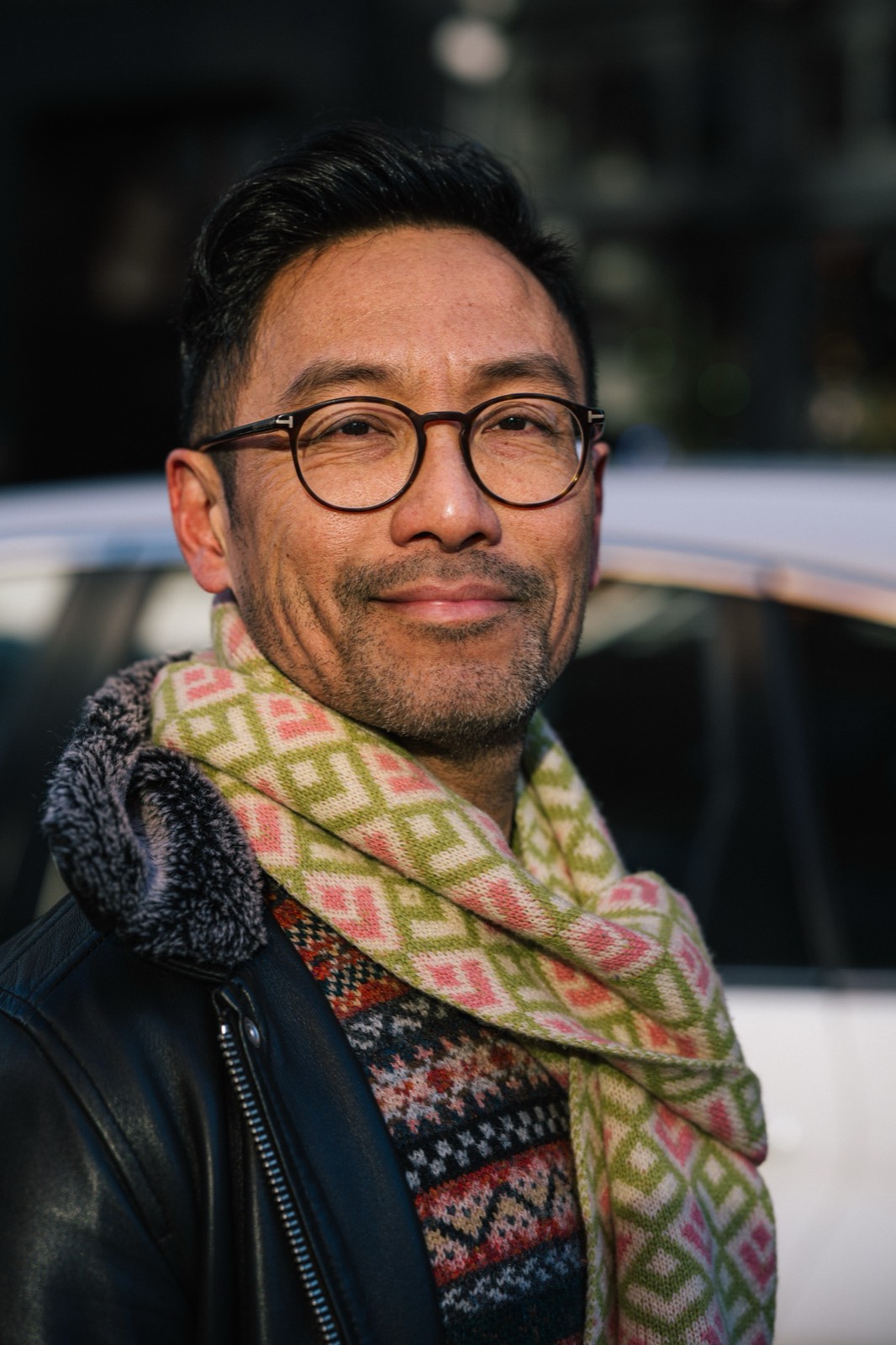 Portrait of a man in glasses and a patterned scarf beside a car