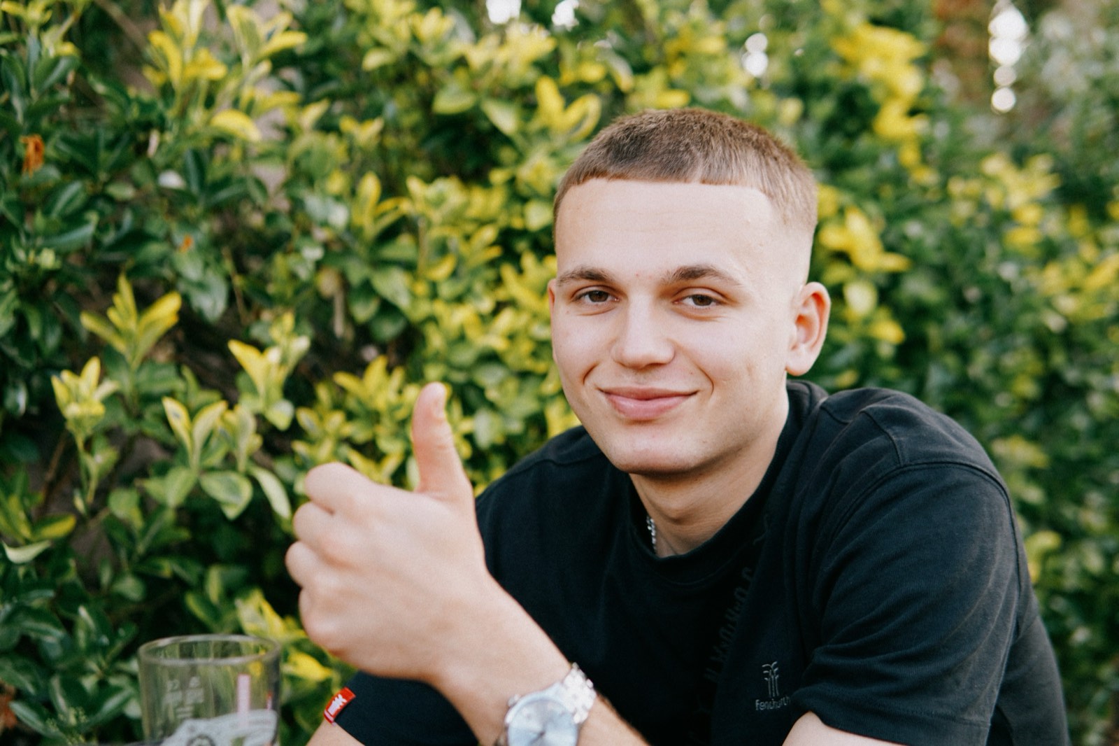 Portrait of a smiling young man in front of green hedges