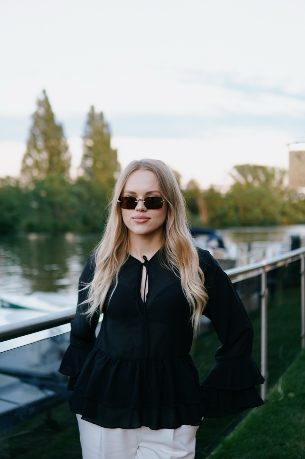 Portrait of a blonde woman in black wearing sunglasses by the river