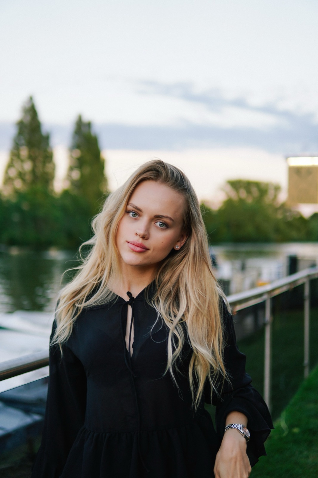 Portrait of a blonde woman in a black dress by the river at dusk