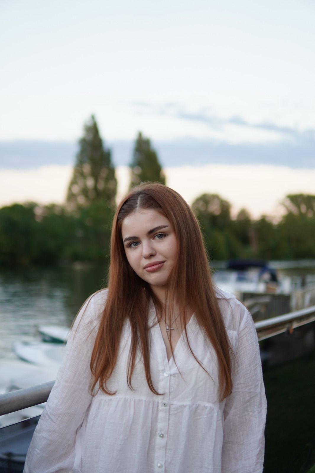 Portrait of a young woman in a white shirt by the river at dusk
